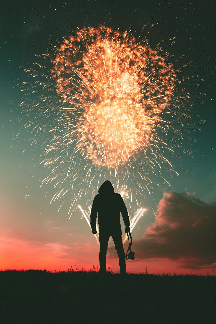 silhouette photo of standing man holding camera looking at fireworks display